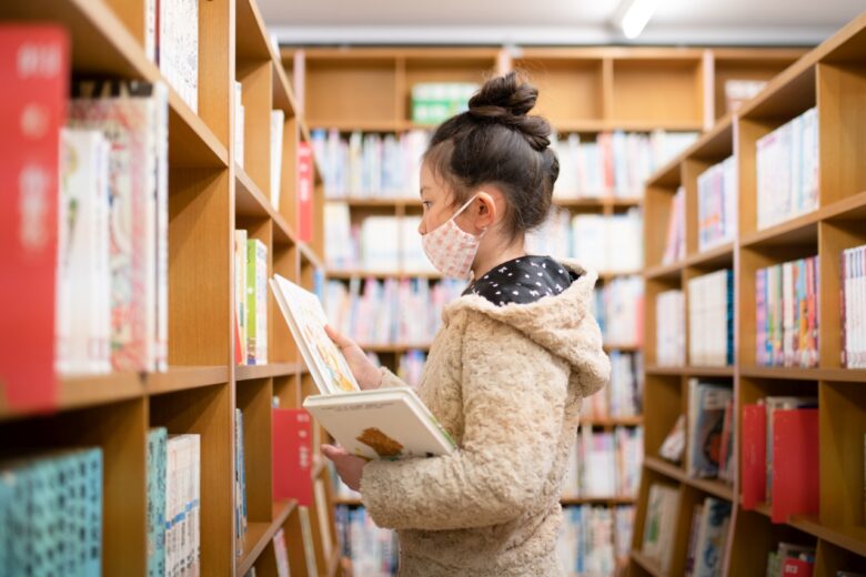 図書館で本を選ぶマスクを着用した少女